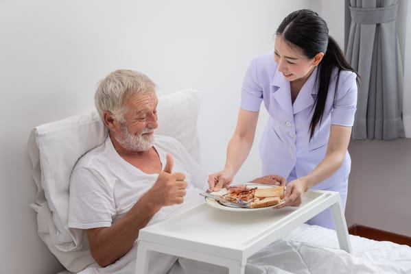 Nurse serving food to a smiling resident in bed