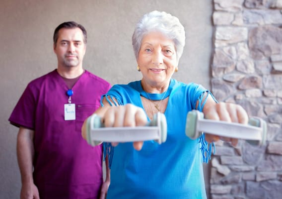 Resident exercising with weights and staff member behind