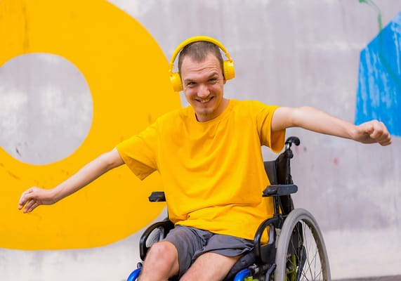 A young man in a wheelchair wearing headphones and smiling