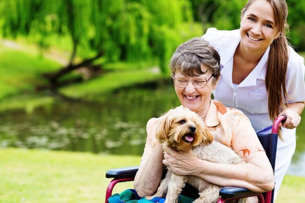 Resident enjoying the outdoors with a staff member and a dog