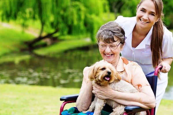 Resident enjoying the outdoors with a staff member and a dog