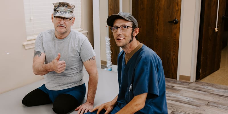 Two men sitting in a room, one giving a thumbs-up