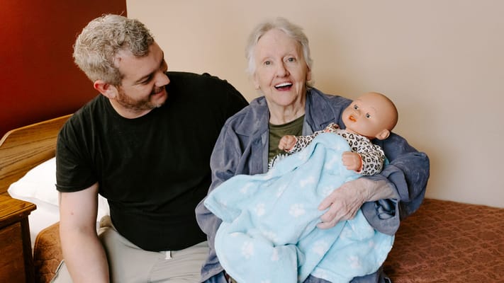 A caregiver and a resident playing with a doll indoors