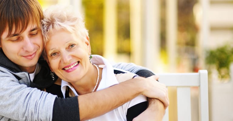 A smiling older woman embracing a young man outdoors