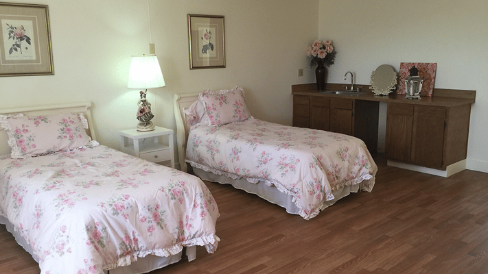 A shared resident room with floral bedding and kitchenette