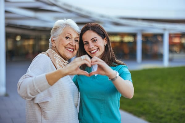 A resident and staff member smiling and making a heart shape
