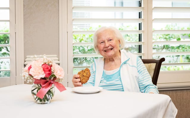 A smiling resident enjoying a cookie by the window