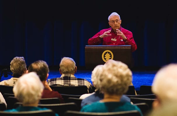 A speaker addressing a group of residents in an auditorium