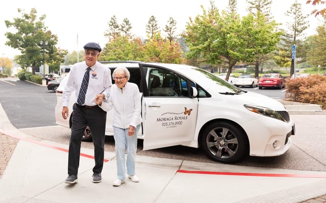 Resident assisted by staff member near facility van