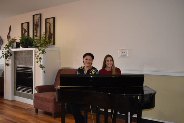 Two women seated at a piano in a common area