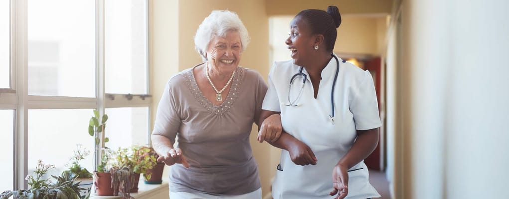 A caregiver assisting a smiling resident in a hallway