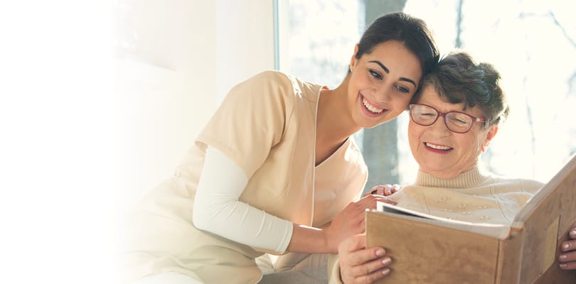 Staff member smiling with elderly resident reading a book