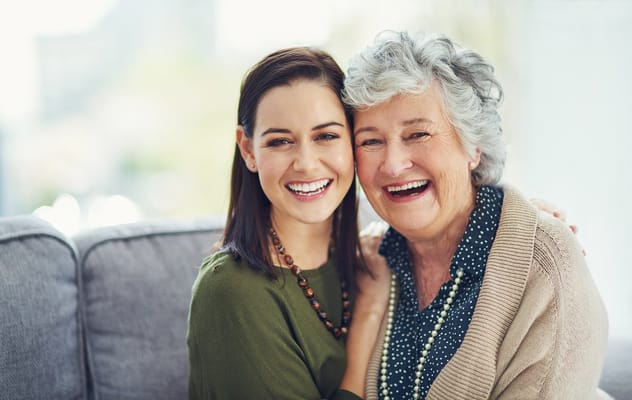A smiling caregiver and resident embracing on a couch