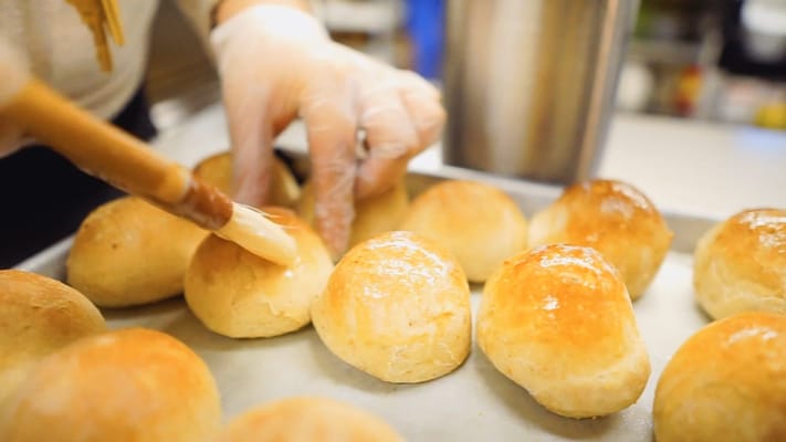 A close-up of freshly baked rolls being brushed with butter
