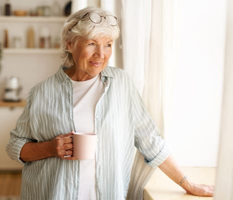 Senior woman holding a pink mug near a window