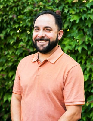Staff member smiling against a green hedge background