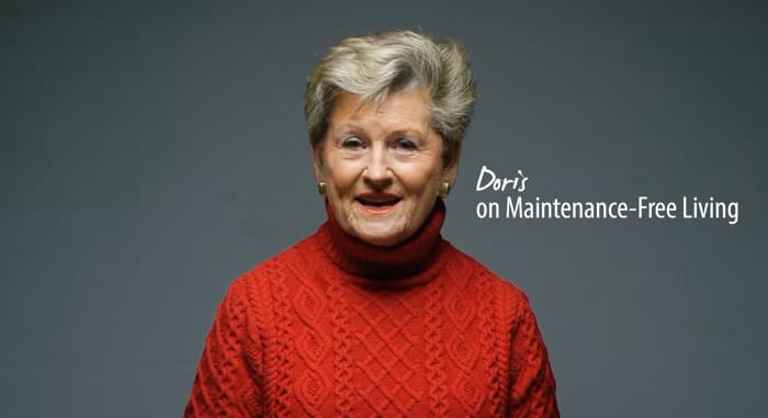 An elderly woman in a red sweater speaking warmly.