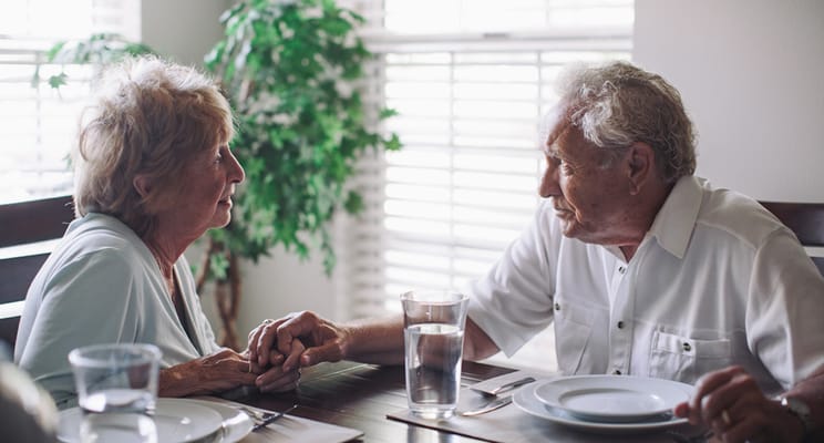 Elderly couple holding hands at a dining table
