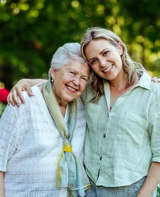 An elderly woman and a caregiver smiling outdoors