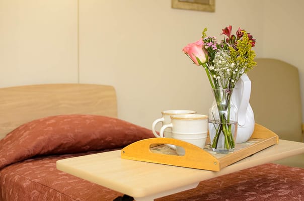 A cozy room with a tray of flowers and cups on a bedside table