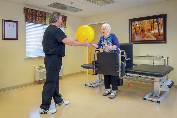 Therapist assisting a resident with a ball in a therapy room