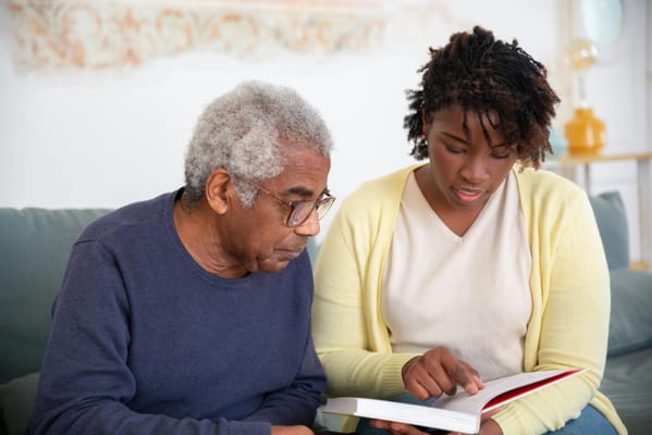 An elderly man and a caregiver reading together