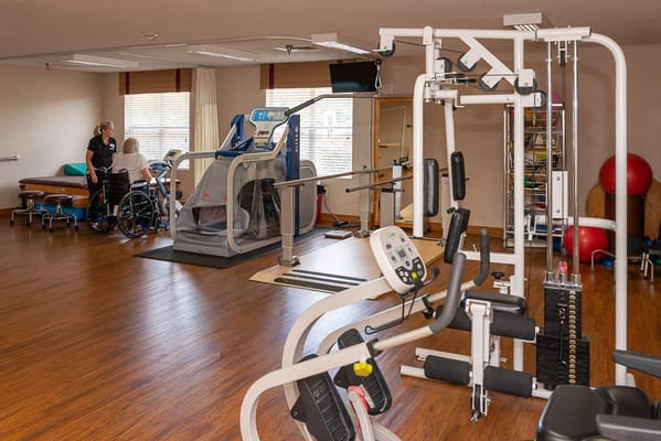 Fitness area with exercise equipment and staff assisting a resident