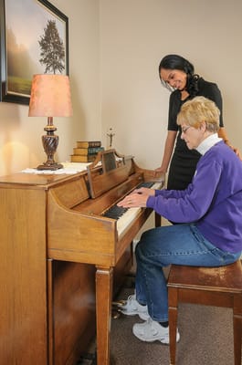 Resident playing piano with staff assistance