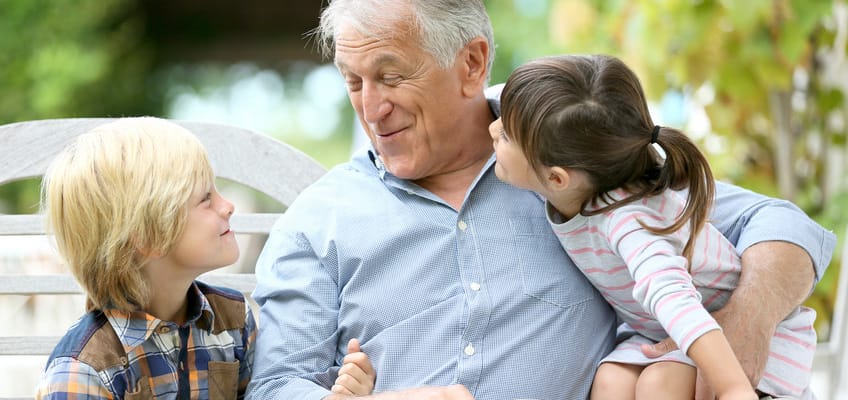 A senior man smiling with two children outdoors