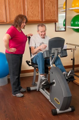 Resident using a recumbent exercise bike with staff assistance