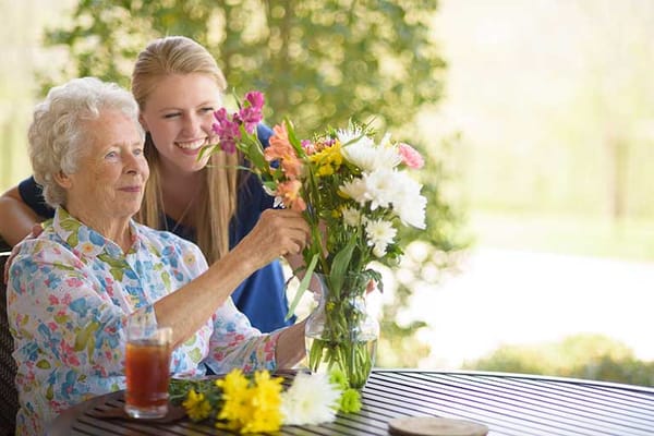 Resident arranging flowers with staff outdoors