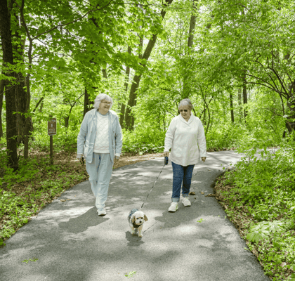 Two elderly women walking a dog on a path in a park