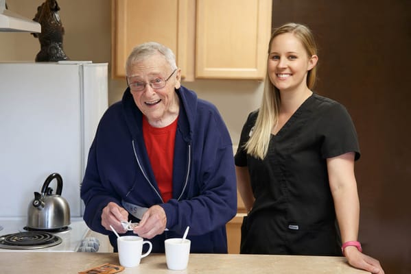 A resident and staff member preparing drinks in a kitchen