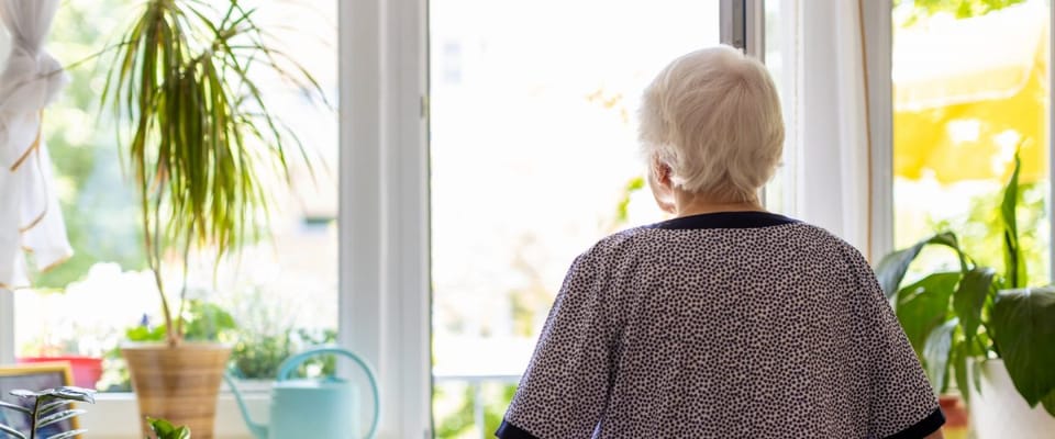 Senior resident looking out a sunny window with plants