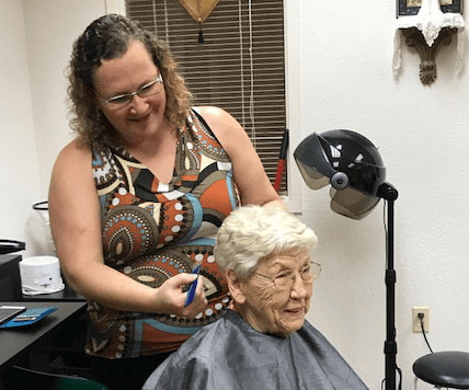 Resident receiving a haircut from staff in a salon.