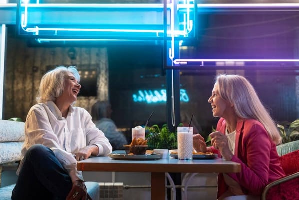 Two women laughing together over drinks and snacks