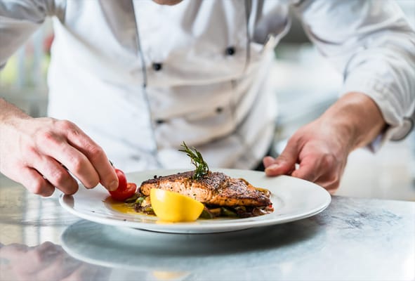 A chef plating a gourmet fish dish with lemon and herbs