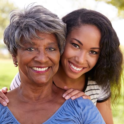 An older woman and a younger woman smiling together outdoors