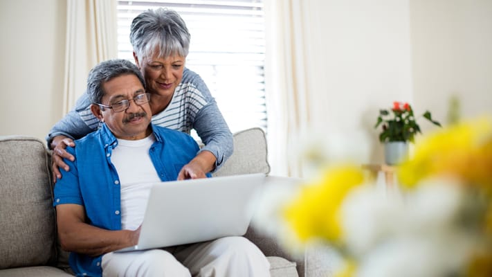 An elderly couple interacting with a laptop in a cozy living room