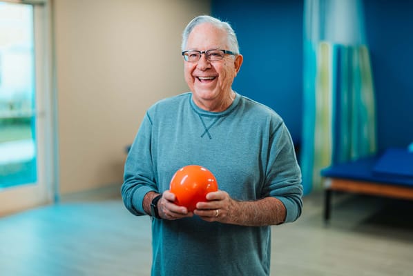 Cheerful senior man holding an orange ball in activity room