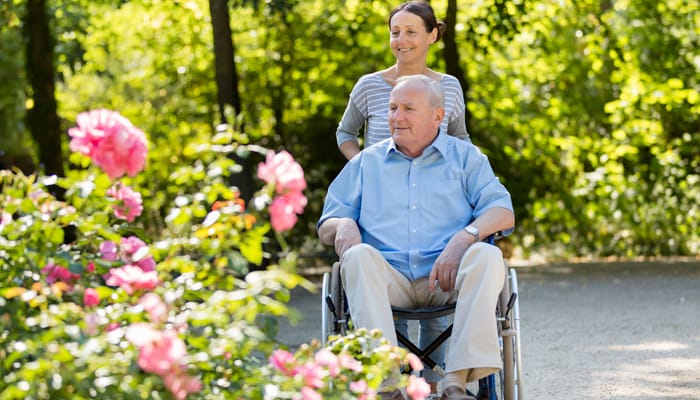 A caregiver pushing a resident in a wheelchair through a garden