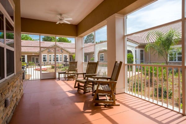 Covered patio area with rocking chairs and view of building