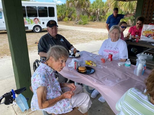 Residents enjoying a meal outdoors with staff assistance.