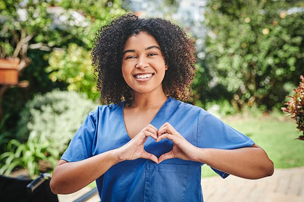 Healthcare worker smiling and making a heart gesture in a garden