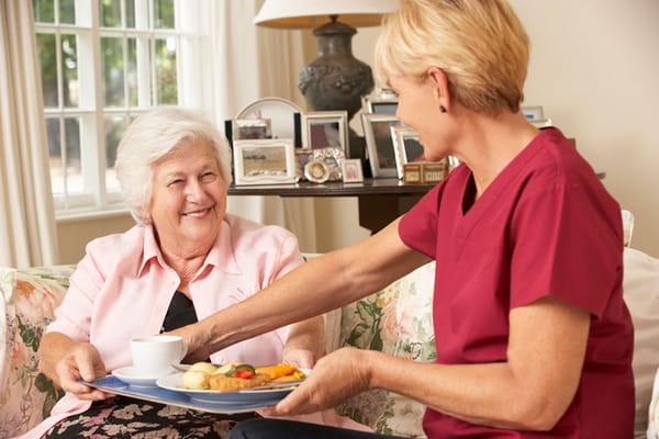 Staff member serving food to a resident in a cozy living area