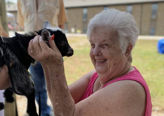 A senior woman holding a goat, smiling