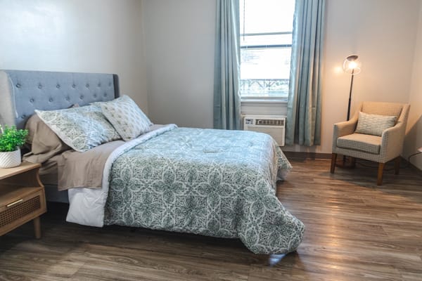 A cozy private resident room with a bed and chair