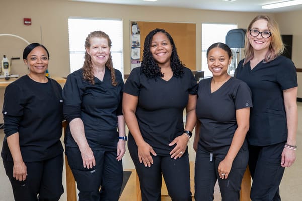 Five staff members in black scrubs smiling indoors