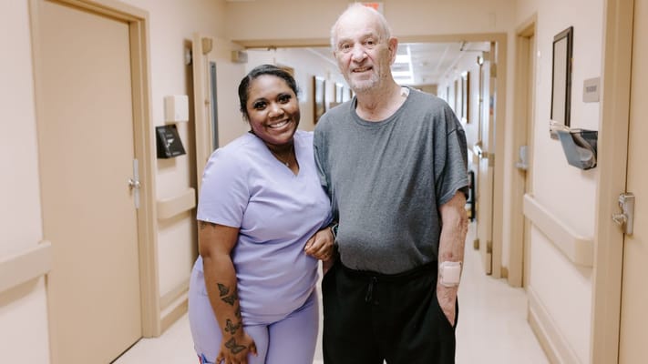 A nurse smiling alongside a resident in a hallway