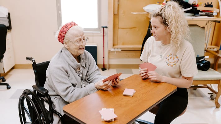 Resident and staff playing cards in an activity room